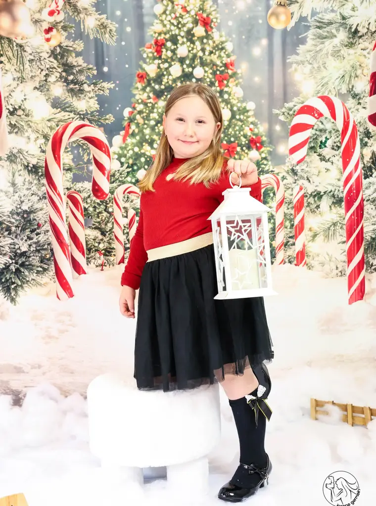Petite fille tenant une lanterne devant un sapin de Noël décoré.