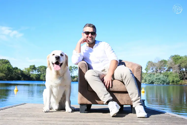 Homme assis dans un fauteuil sur un ponton, son labrador à côté, au bord d'un lac.